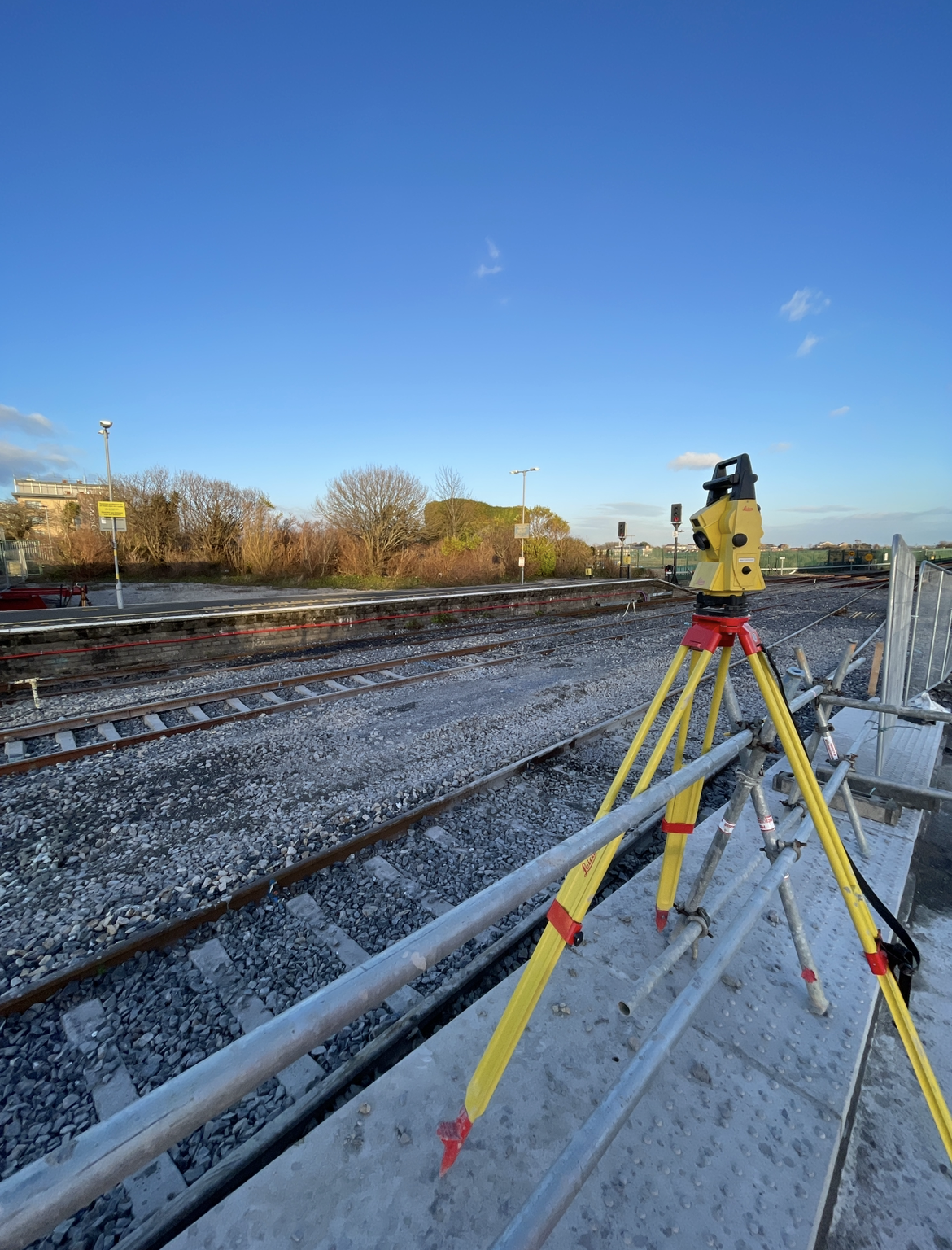 Leica total station set up on a tripod overlooking rail tracks at dusk